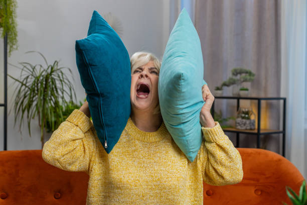 Разочарованная женщина в желтом свитере кричит и держит две подушки на диване в современной гостиной.