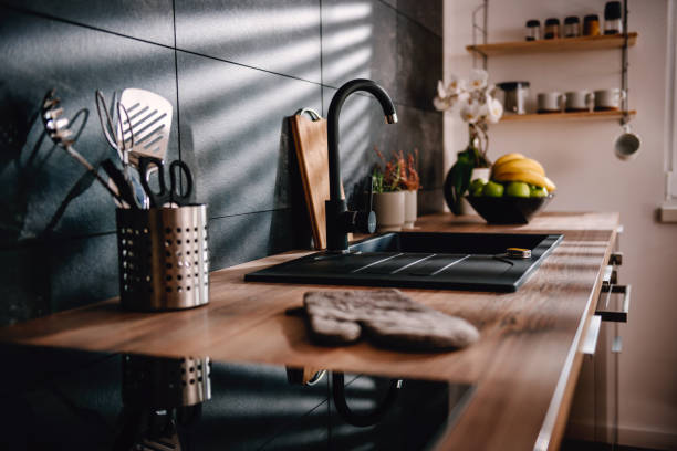 Современный интерьер кухни с деревянными столешницами и стильной темной плиткой, раковиной, посудой и свежими фруктами.