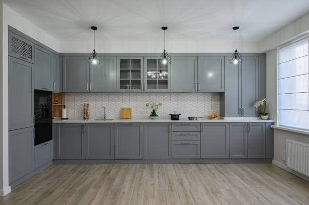 Современная кухня с серыми шкафами, бытовой техникой из нержавеющей стали, фартуком в елочку и подвесным освещением.